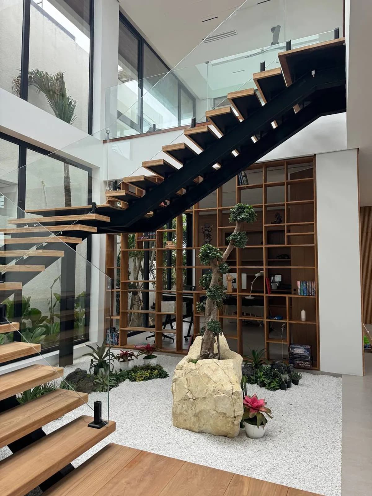 Floating timber staircase on a black steel spine over an indoor rock garden